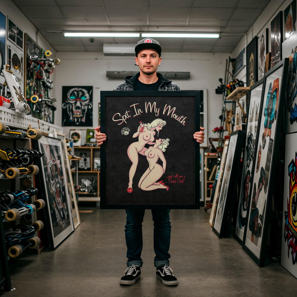 A man is standing in a room filled with various artworks, holding a framed piece of art that features a nude woman.