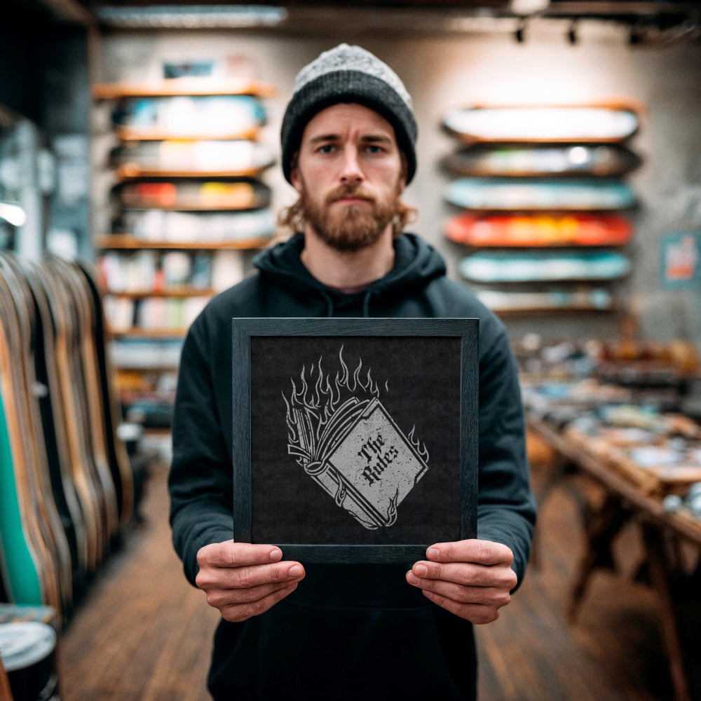 A man with a beard is holding a black frame with a white and black graphic design on it, which appears to be a book with flames on it.