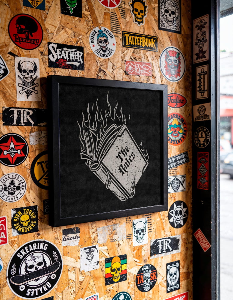a wall covered in various stickers, patches, and graffiti, including a framed image with a burning book and the text "The Rules".