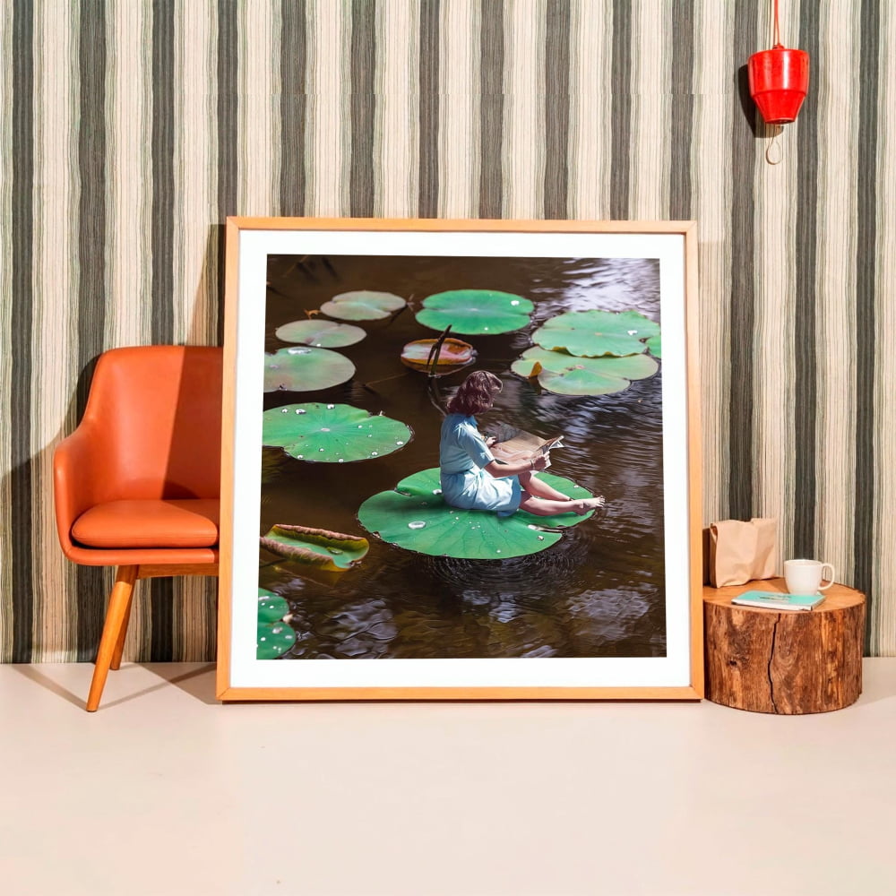 A framed photograph of a person sitting on a lily pad in a pond, surrounded by lily pads.