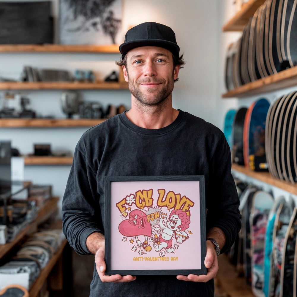 A man is holding a framed picture with a cartoon-style illustration of a woman and a heart.