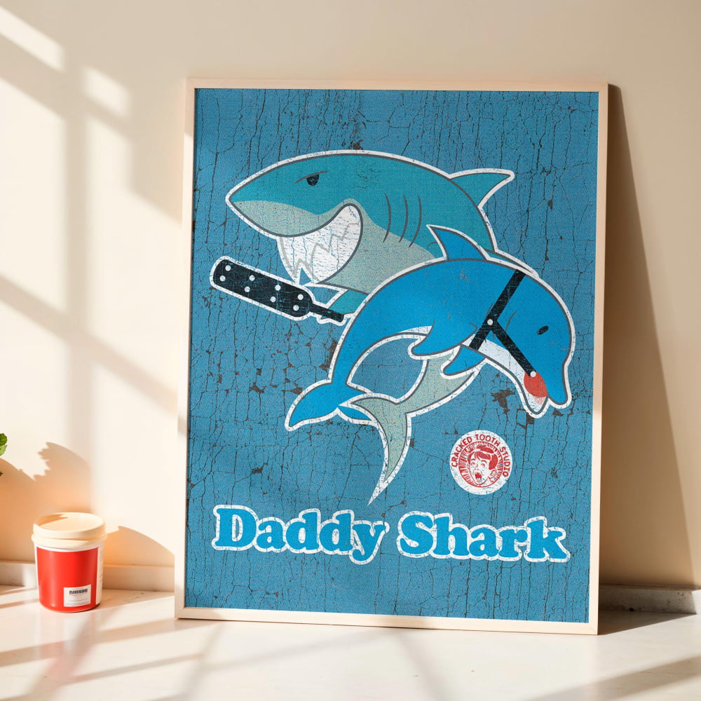 A framed poster featuring a cartoon image of a blue shark and a dolphin, with the text "Daddy Shark" below the illustration.