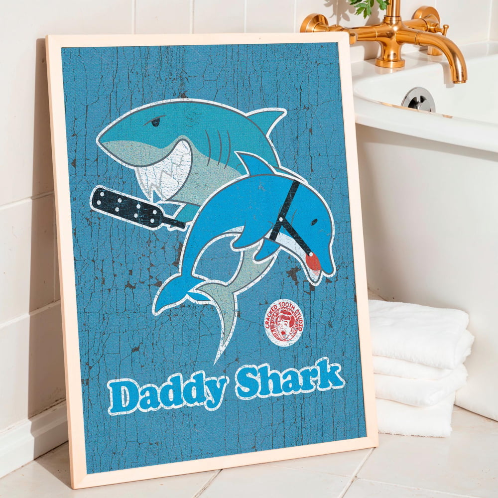 A framed poster with a cartoon image of a blue shark and a dolphin, along with the text "Daddy Shark" on a blue background.