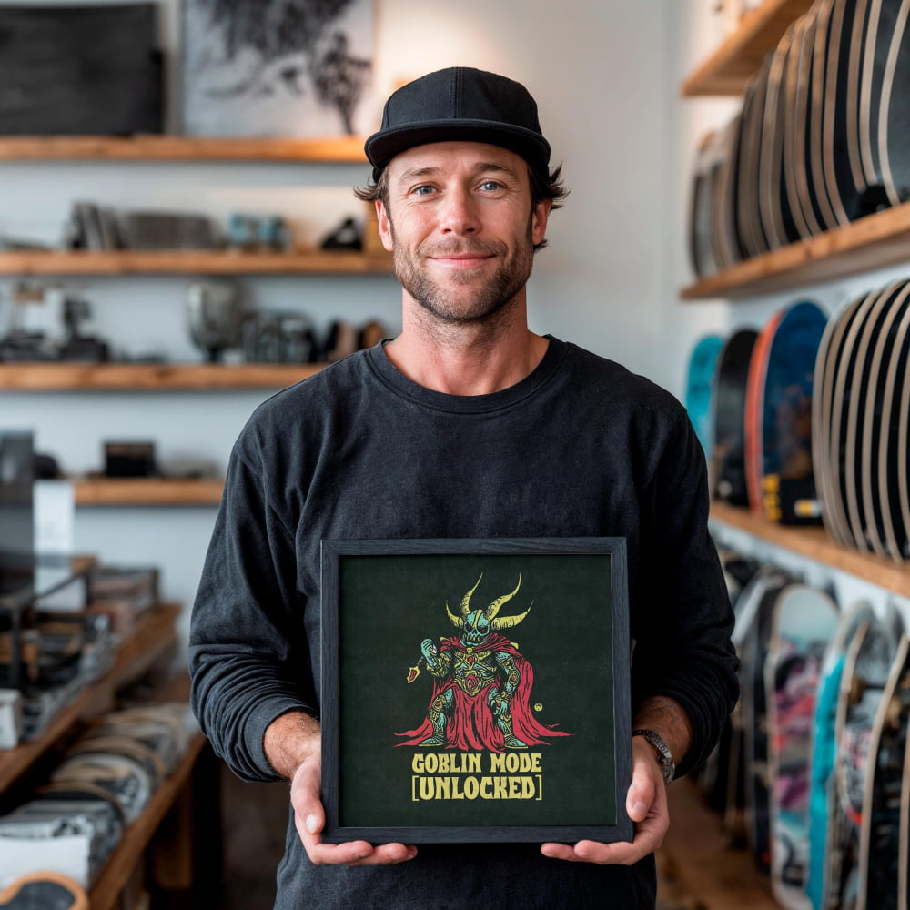 A man is holding a framed artwork featuring a character with horns and a red cape, which appears to be a depiction of the "Goblin Mode Unlocked" character.