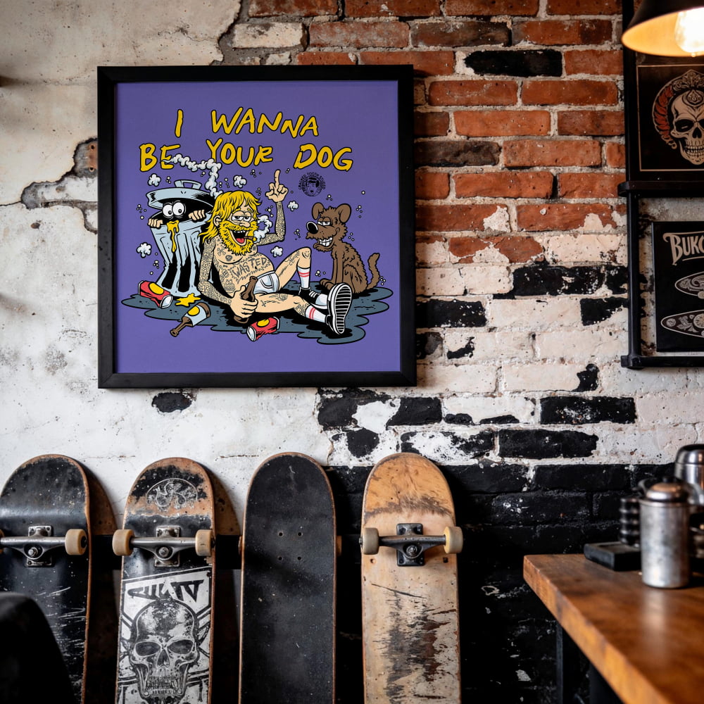 a framed cartoon-style illustration of a man with a dog, accompanied by the text "I WANNA BE YOUR DOG" on a purple background. The illustration is displayed on a brick wall, with several skateboards leaning against the wall in the foreground.