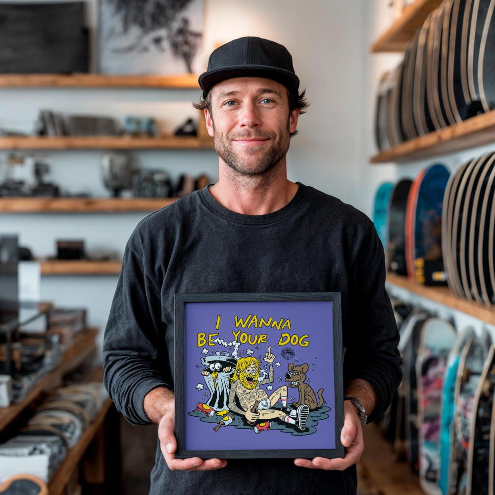 A man is holding a framed picture with a cartoon-style illustration of a dog and a cat, along with the text "I WANNA BE YOUR DOG".