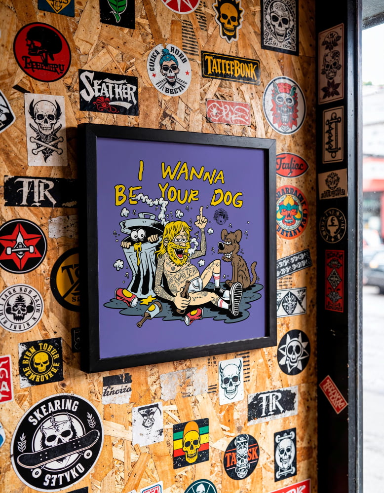 a wall covered in various stickers, posters, and graffiti, including a framed cartoon-style illustration of a person with a dog.