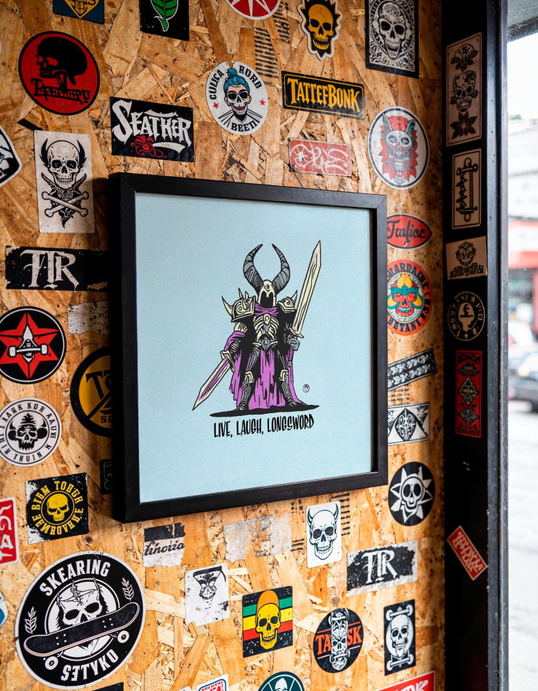 a wall covered in various stickers, patches, and graffiti, including a framed illustration of a character with horns and a sword.