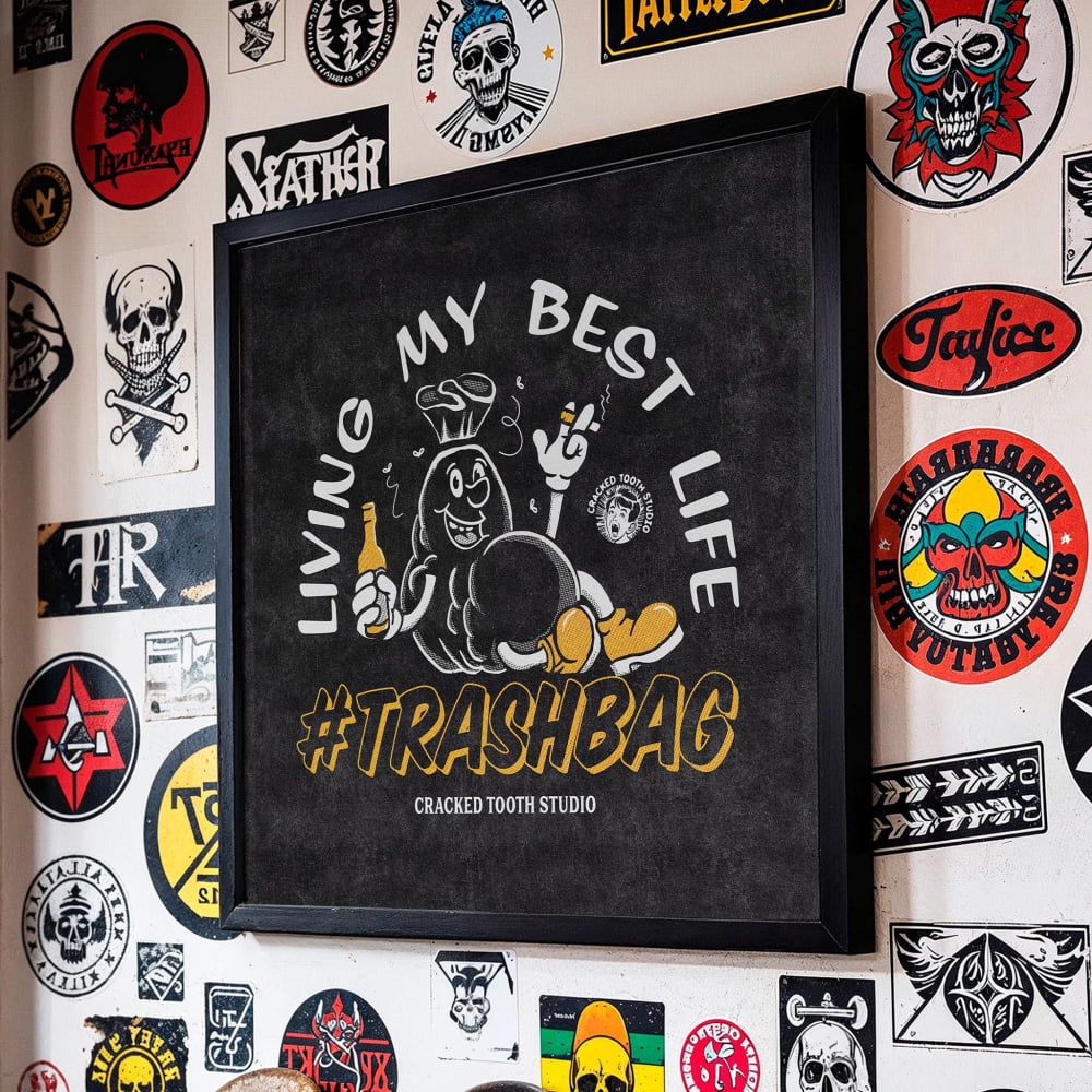 a wall adorned with a variety of stickers and graffiti, including a prominent black and white sticker with a cartoon character and the text "Living my best life #TRASHBAG" and "Cracked Tooth Studio".