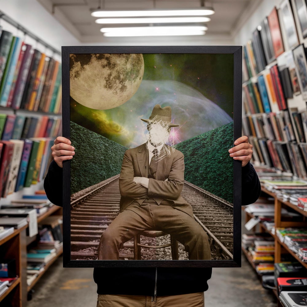 A person is holding up a framed image of a man sitting on train tracks, with a large moon and colorful sky in the background.