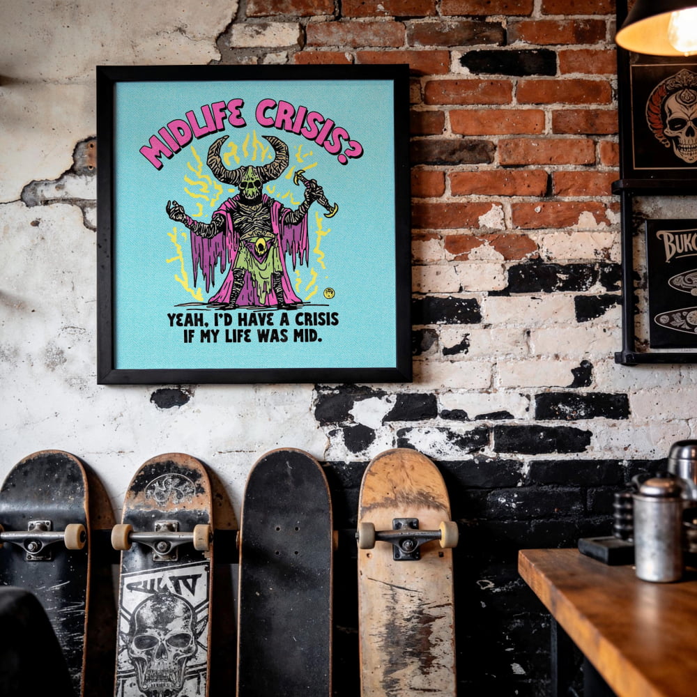 a framed poster with a colorful illustration of a character with horns and a bat-like figure, along with the text "MIDLIFE CRISIS? YEAH, I'D HAVE A CRISIS IF MY LIFE WAS MID." The poster is displayed on a brick wall, and there are several skateboards leaning against the wall.