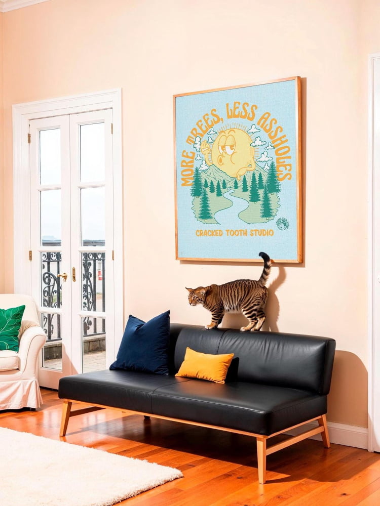 A cat is standing on a black couch in a living room, with a framed poster of a cat and a landscape on the wall above it.