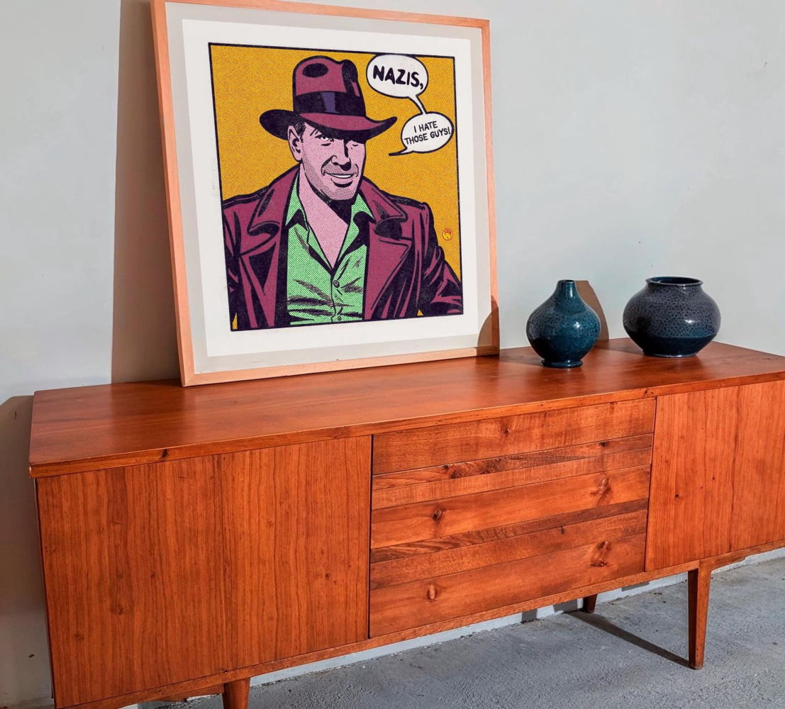a wooden cabinet with a framed pop art-style illustration of a man wearing a fedora and a green shirt, along with a speech bubble that says "NAZIS. I HATE THOSE GUGS!"
