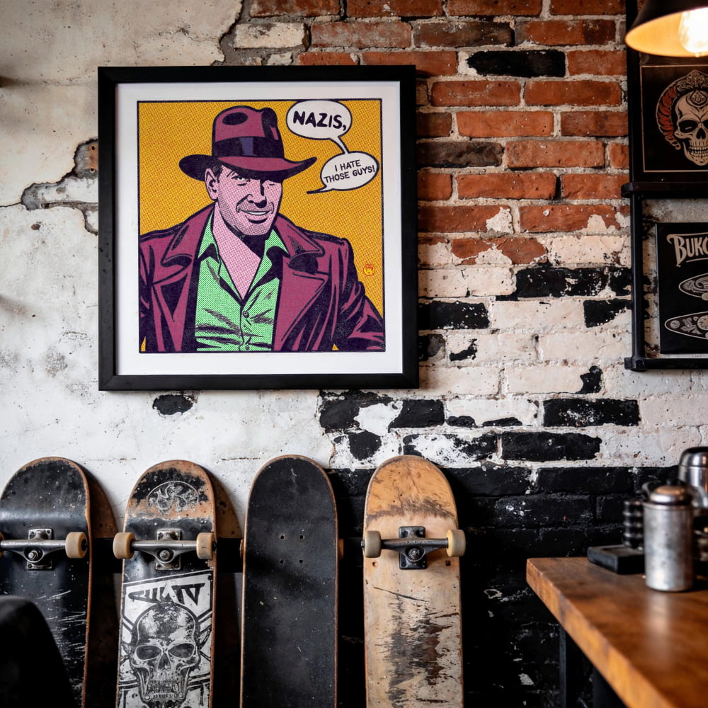 a framed illustration of a man wearing a fedora and a suit, with the caption "NAZIS, I hate those guys!" The image is displayed on a brick wall, with several skateboards leaning against it.