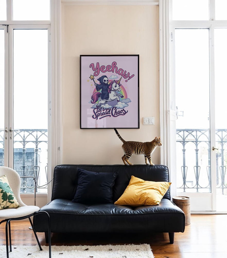 A cat is standing on a black leather couch in a living room, with a framed poster featuring a cartoon character above it.