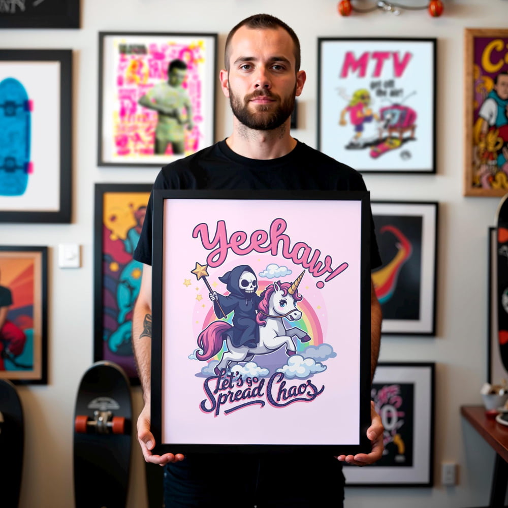 A man is holding a framed poster with a cartoon-style illustration of a skeleton riding a unicorn, with the text "Yeehaw! Let's spread chaos!" The poster is surrounded by various other framed images on the wall.