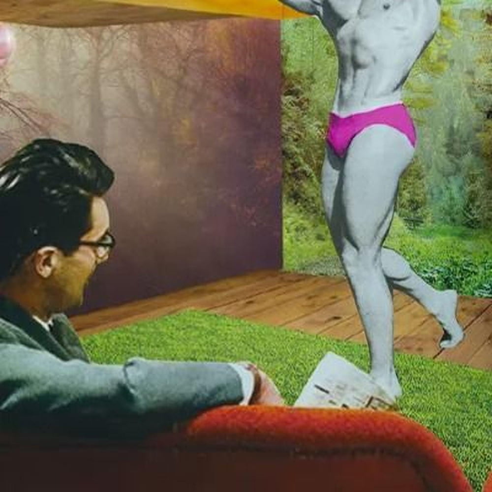 A young man with curly hair and glasses is holding a framed picture of a woman in a red dress, standing in a room with various colorful posters and artwork on the walls.