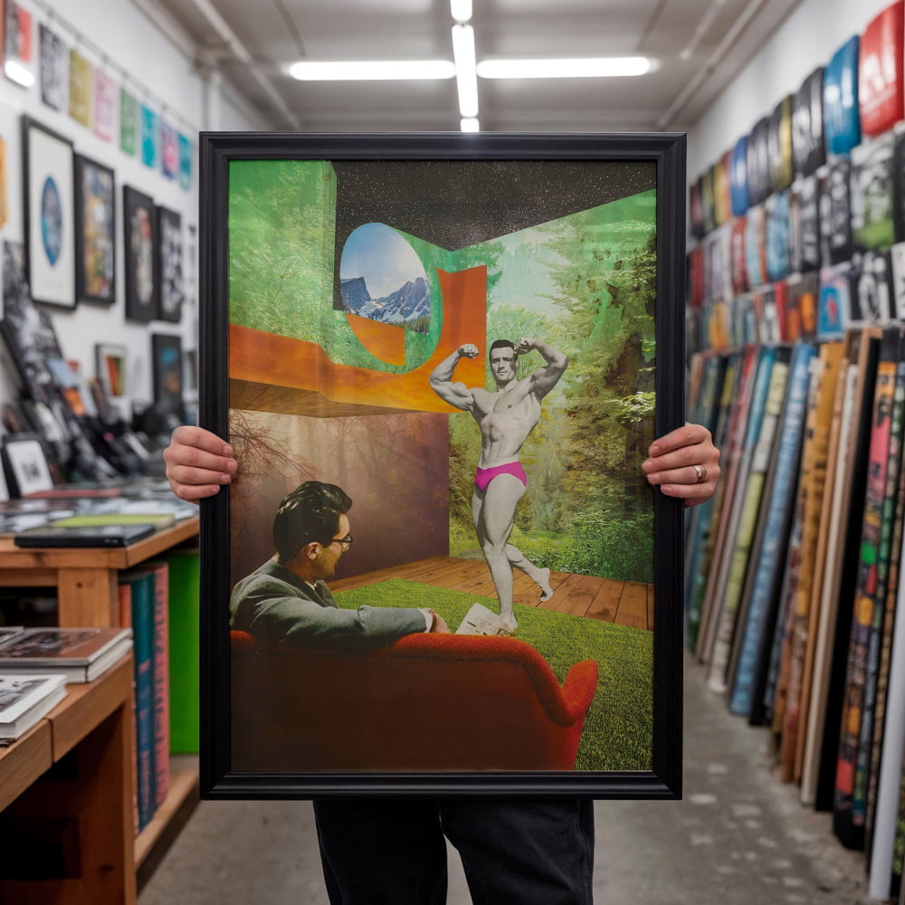 A person is holding up a framed collage of two images. The collage depicts a man in a red shirt and pink underwear flexing his muscles, while another man is sitting on a couch in a room with a mountain landscape in the background.