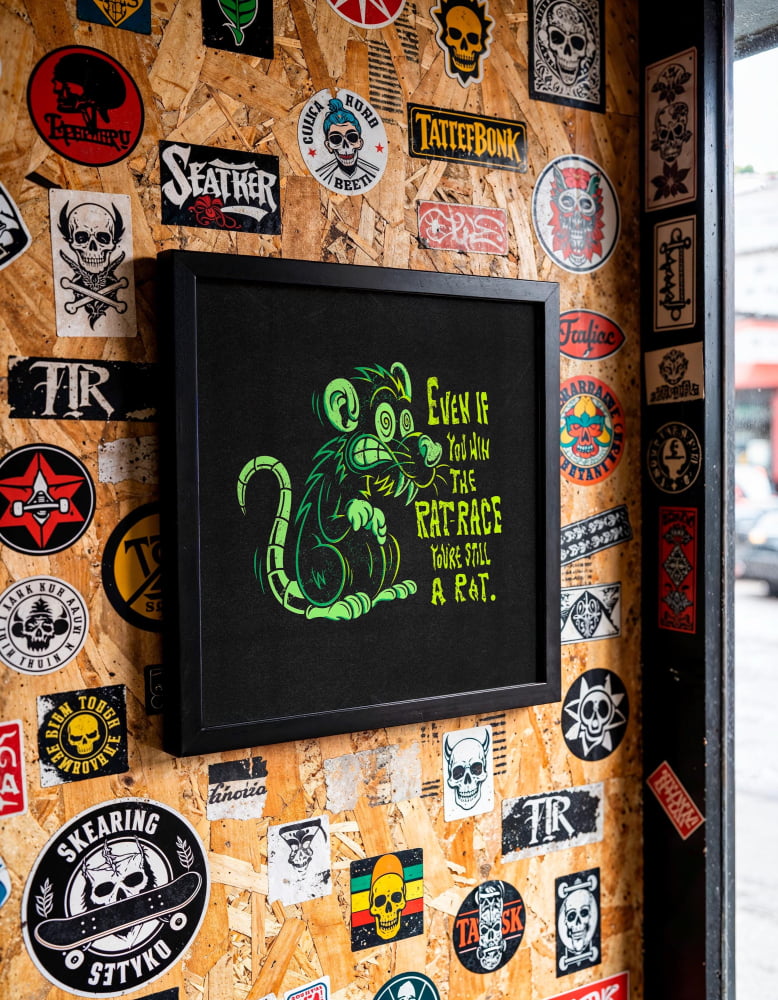 a wall covered in various stickers, patches, and graffiti, including a framed image of a rat with a humorous caption.