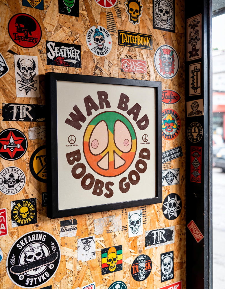a wall covered in various stickers, posters, and patches, including a prominent poster with the text "WAR BAD BOBS GOOD" and a peace symbol.