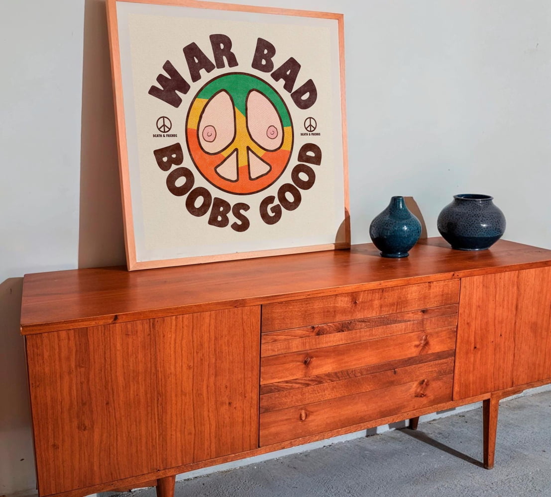 a wooden cabinet with a framed poster on top of it, which displays a peace symbol and the text "WAR BAD BOBS GOOD". There are also two blue vases placed on the cabinet.