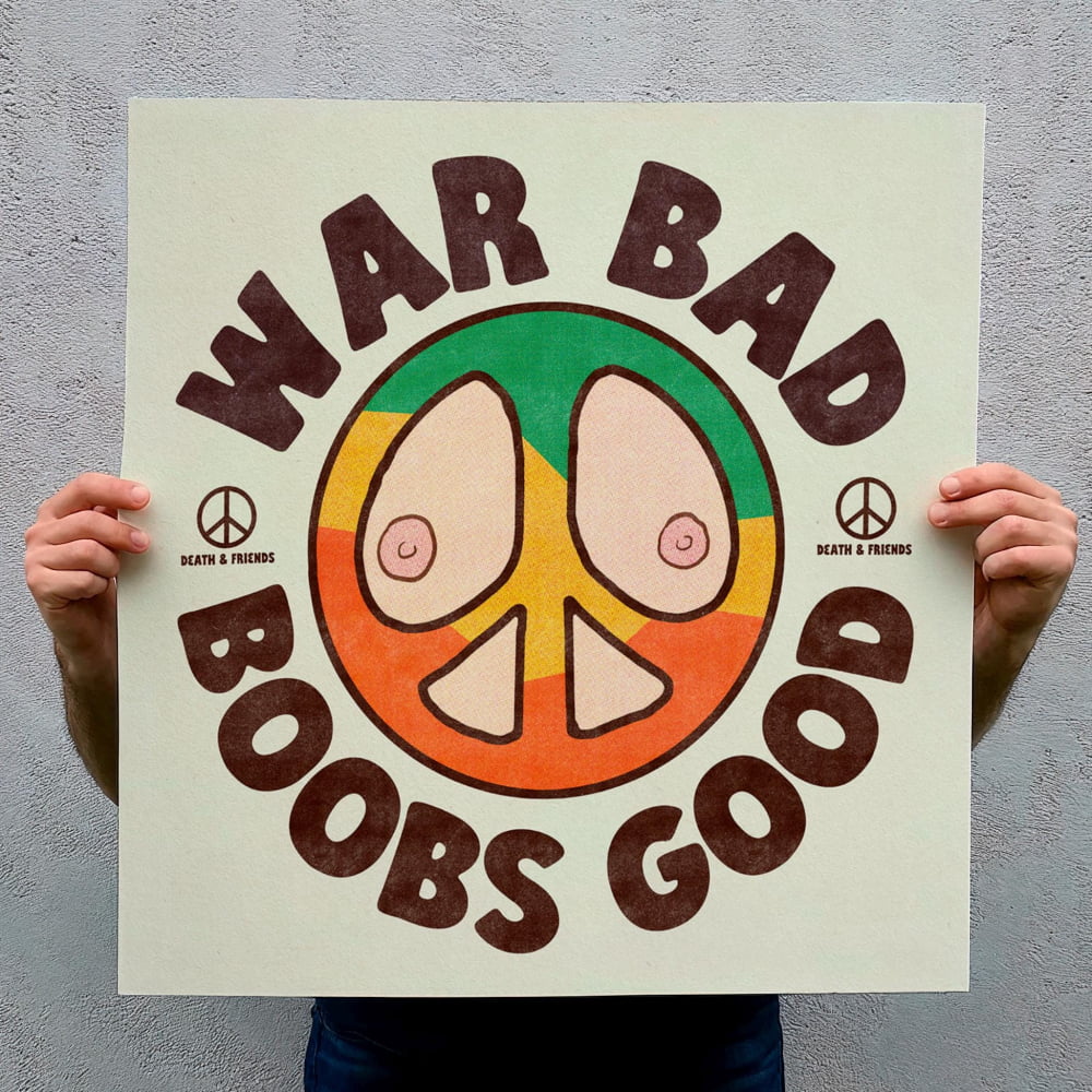 A person is holding up a sign with a peace symbol and the text "War Bad Boobs Good" written on it.