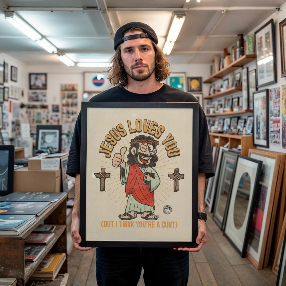 A man is holding a framed poster with a cartoon image of Jesus and the text "JESUS LOVES YOU (BUT I THINK YOU'RE A CUT)" in a room filled with various items.