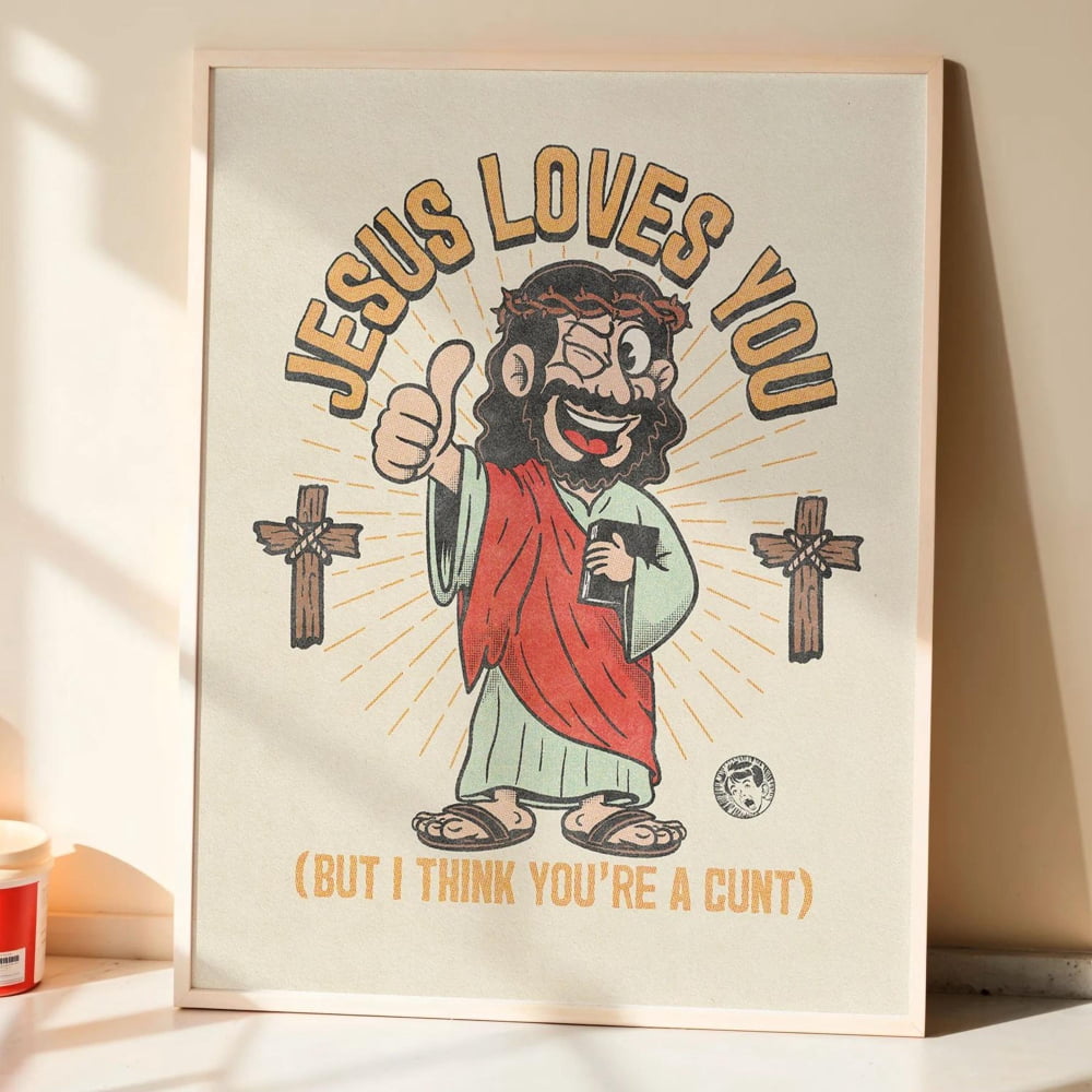 A framed poster with a cartoon depiction of Jesus wearing a crown and holding a book, along with the text "JESUS LOVES YOU" and "(BUT I THINK YOU'RE A CUT)" below.