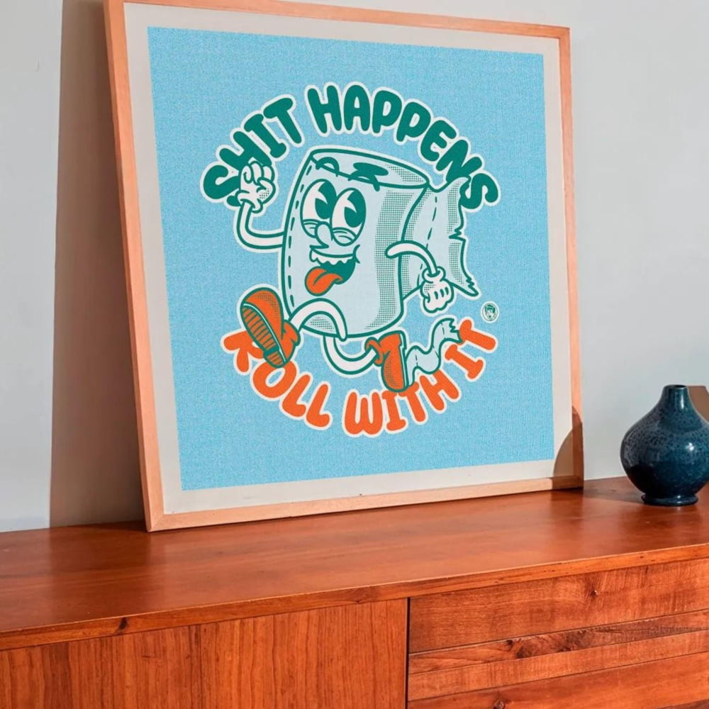 a wooden cabinet with a framed poster of a cartoon character on top of it. The poster has a humorous message that reads "SHIT HAPPENS ROLL WITH IT". There are also two vases placed on the cabinet, one on the left side and the other on the right side.