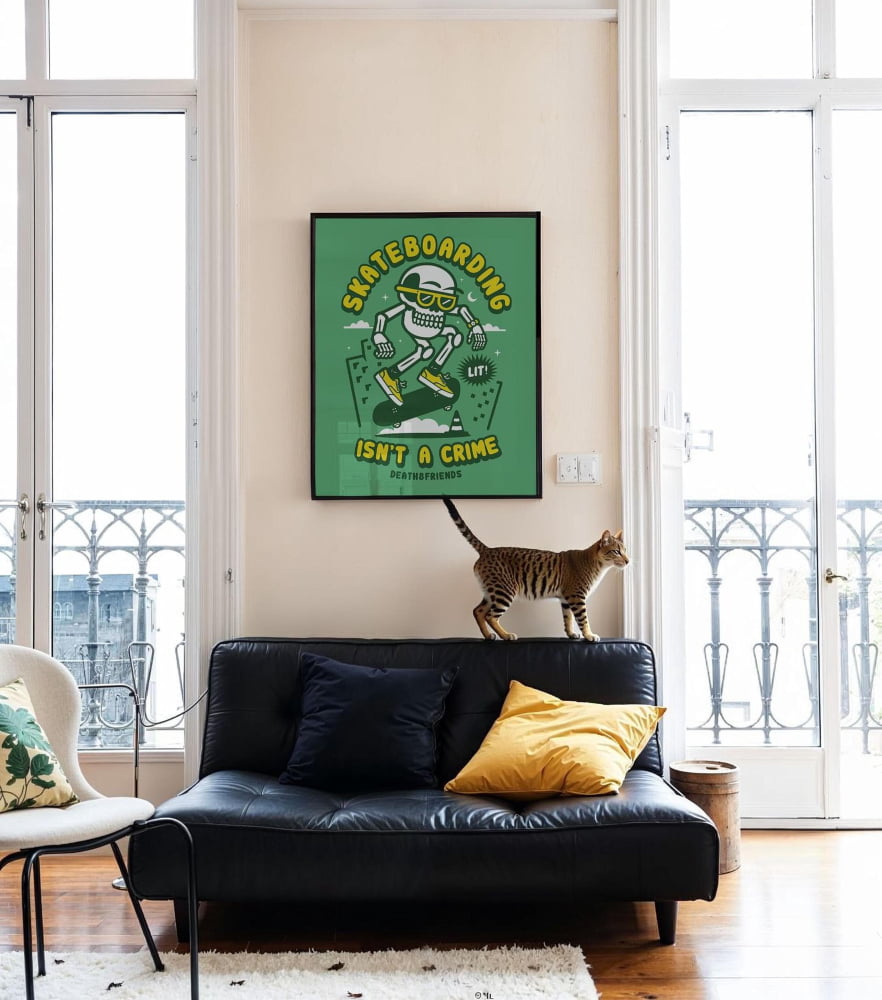 A cat is standing on a black leather couch in a living room, with a framed poster of a skeleton skateboarder above it.