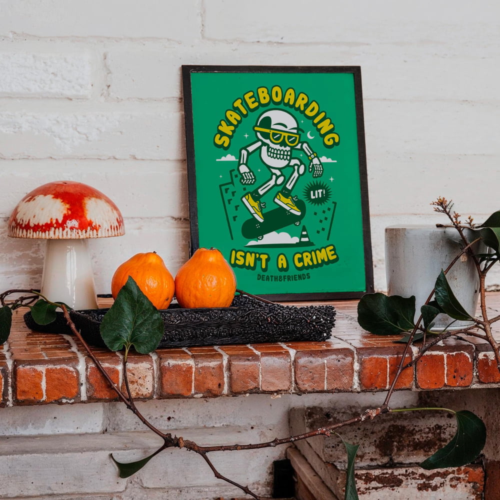 a framed poster with a cartoon skeleton skateboarding, accompanied by a mushroom, oranges, and a plant on a brick shelf.