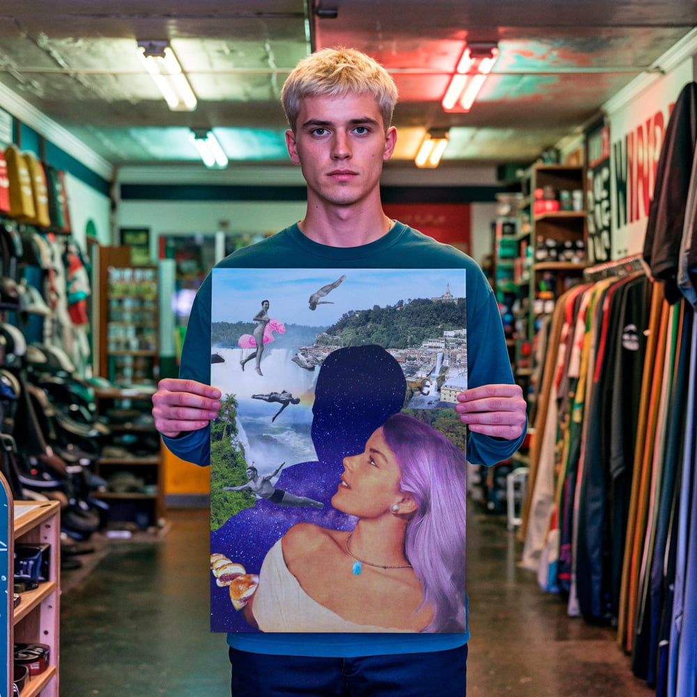 A young man stands in a clothing store, holding up a framed collage of various images, including a woman's face and a landscape scene.