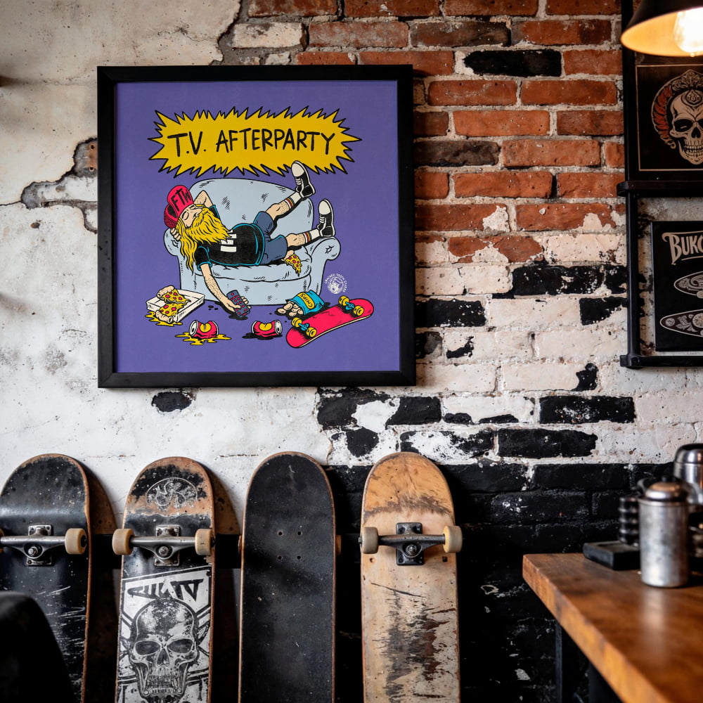 a wall with a framed cartoon-style illustration of a person lounging on a couch, surrounded by skateboards.