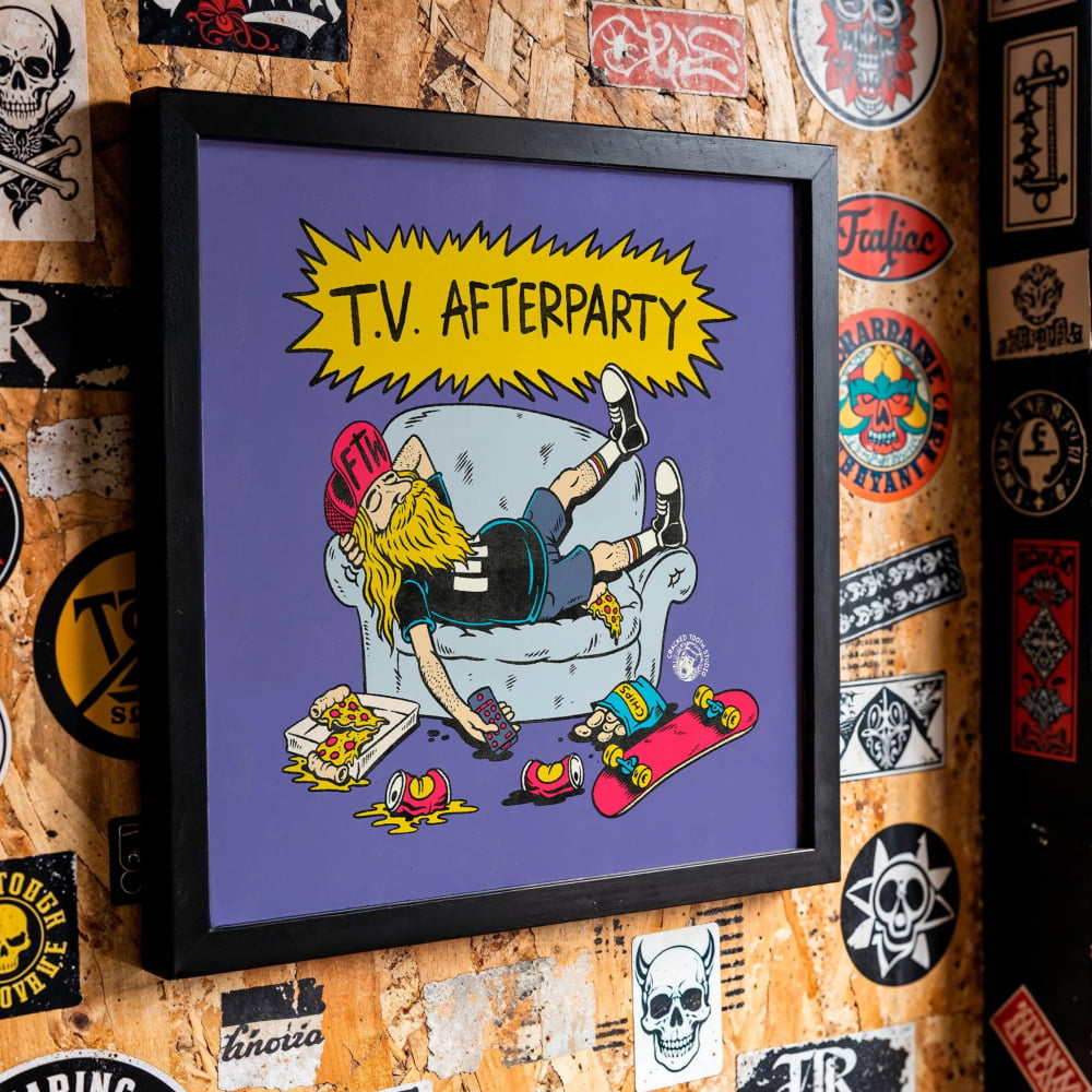 a wall covered in various stickers, posters, and graffiti, including a framed cartoon illustration of a person sitting on a couch with skateboards around them.