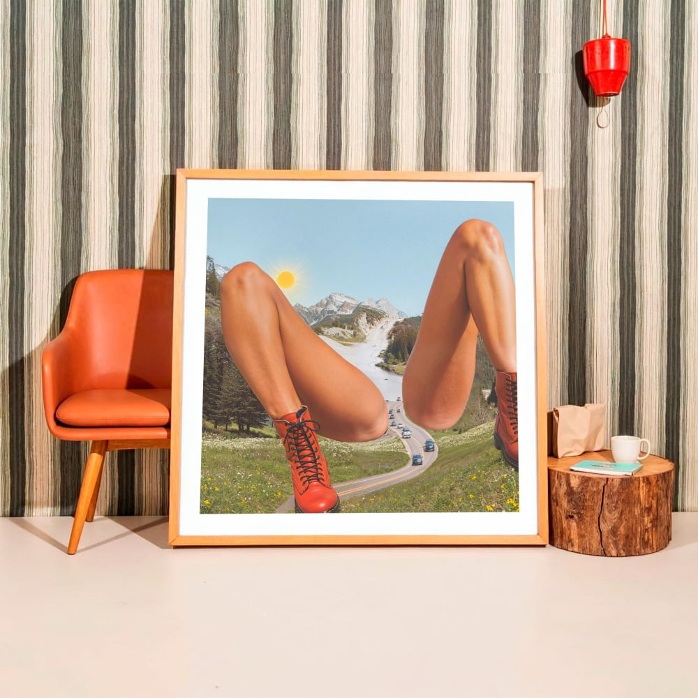 a large framed picture of a person's legs in a surreal landscape, with a road and mountains in the background.
