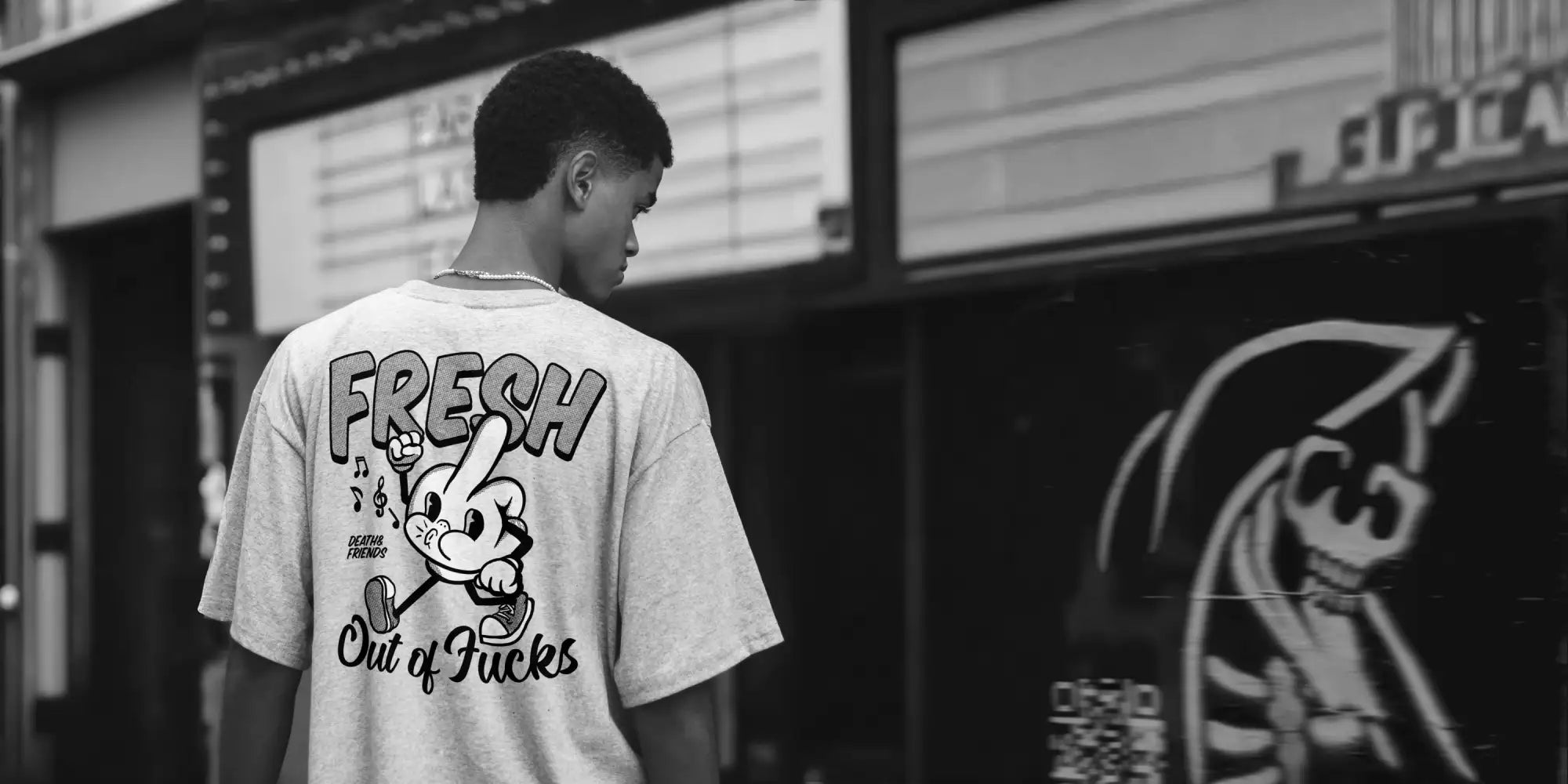 A black-and-white graphic tee featuring a cartoon character with the text ’fresh’ and ’out of fucks,’ worn by an individual.