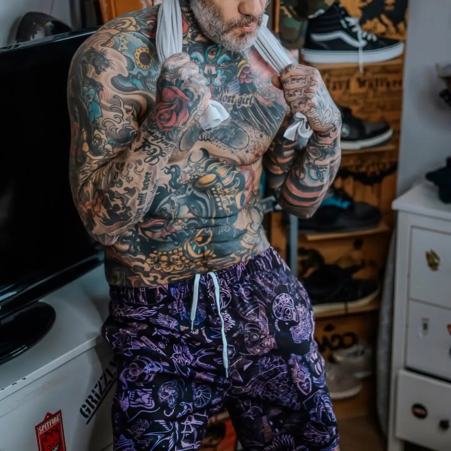 Tattooed man wearing purple and black patterned shorts with white drawstring.